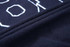 A close-up of a navy collegiate jacket fabric featuring textured lettering and stitched details.