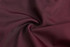A maroon fabric swirled together, showcasing its smooth texture and vibrant colour, with a branding logo visible.