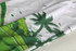 Track suit pants in white and green featuring a palm tree design and abstract splashes of colour, with a logo on the waistband.
