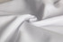 A close-up of white fabric, showcasing its smooth texture and folds. The image features a subtle sheen.