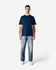 A model wearing a navy blue Gildan Softstyle T-shirt paired with light blue jeans. The T-shirt has a logo on it.