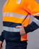 A high-visibility jumper featuring bright orange and navy blue with reflective stripes. It includes a side pocket and has a logo.
