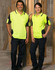 Two individuals stand in high-visibility yellow safety polo shirts with navy accents, inside an unfinished building.