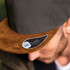 A cap featuring a dark grey crown and a brown suede brim, with a logo on the side.