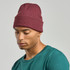 A maroon beanie worn by a person in a teal shirt, featuring a logo on the front.