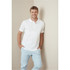 A man wearing a white premium cotton polo shirt, smiling while leaning against a wall, paired with light blue trousers.