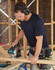 A navy blue short-sleeve work t-shirt worn by a man using a circular saw at a construction site.