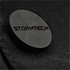 A close-up of a dark textured fabric featuring a circular black logo with the word "STORMTECH."