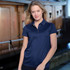 A woman in a navy polo shirt stands near a boat, displaying a logo on the garment.