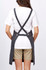 A grey bib apron worn over a white t-shirt, featuring crossed back straps and a casual fit.