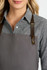 A ladies long sleeve button-up shirt in grey, featuring brown leather straps on an apron. It has a logo.