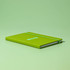 A green A5 notebook with an elastic band and a simple logo on the cover, resting on a matching green surface.