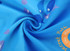 A blue beach towel with a double-faced pile featuring playful fish designs and circular motifs. It has a branding logo.