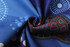 A folded piece of fabric featuring vibrant blue tones with intricate patterns in red and white dots. It has a logo.