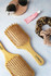 A bamboo hairbrush in a light wooden finish, accompanied by sunglasses, lip balm, and a hair scrunchie.