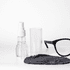 An eye glass cleaner set featuring a spray bottle, a clear container, a black cleaning cloth, and a pair of black glasses.