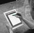 A person using a black stylus pen on a tablet, with a light-coloured background. The stylus has a sleek design and branding.