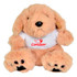A soft, beige plush puppy sitting upright, featuring a white shirt with a logo. Its paws and ears are dark brown.