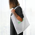 A white recycled PET bag is held by a person with tattoos, featuring a logo printed in green.