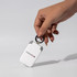 A white mini power bank with a keyring attachment is held by a hand, featuring a logo on its side.
