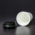 A white coffee mug made from recycled materials, featuring a black lid, displayed on a dark background.