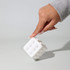A white cube toy with rounded dots, being held by a hand, set against a light background.