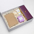 A gift box containing a brown notepad, a round item, a cream tube, a purple candle, and an item with a logo.