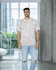 A man stands wearing a bleach-out dyed T-shirt in neutral tones, paired with ripped blue jeans.