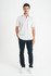 A man wearing a white short sleeve button-up shirt with a chest pocket, paired with dark trousers and white shoes.