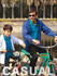 A blue kids' yachtman's jacket with lining displayed on a child and an adult, both on bicycles near a water body.