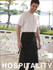 A man in a white t-shirt wears a black polyester drill three-quarter apron with a pocket, standing outdoors.