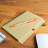 A brown spiral-bound notebook with a kraft paper cover and an orange Matador pen resting on top, placed on a wooden surface.