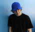 A blue cotton and spandex cap worn by a person in a black t-shirt, leaning against a blue wall.