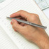 A metal pen in a person's hand, writing in a lined notebook. The pen is silver in colour.