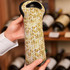 A drink bottle holder with a woven, straw-like pattern in natural tones, featuring a black top and branding.