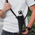 A drink bottle sling bag in black, featuring a logo, worn across a person's body with a stainless steel bottle inside.