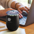 A drink bottle in matte black with a clear lid, placed on a table beside a laptop. It features a logo.