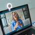 A white Halo Selfie Light attached to a laptop, illuminating a person on a video call. The scene features a modern interior.