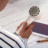 A handheld white cooling fan with a curved design, being held next to a tablet and a pen on a wooden surface.