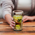 A drink bottle featuring a double wall design, holding green liquid and lime slices, clear glass with a branding logo.