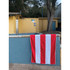 A red and white striped cotton beach towel hangs over a stone wall near a swimming pool.