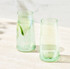 Two green highball glasses, one filled with a drink and garnished with lime, set against a light surface.