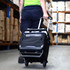 A black rolling cooler with a handle and wheels being pulled in a storage area, featuring a logo.