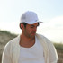A man wearing a white mesh-backed cap and a light-coloured shirt, gazing downward in a natural setting.