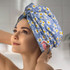 A woman wearing a light blue hair towel decorated with white daisies and yellow accents, featuring a logo.