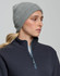 A grey cable knit beanie displayed on a model wearing a navy zip-up top, featuring a logo on the beanie.