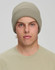 A roll-up cable knit snug beanie in a light khaki colour, worn by a model with short hair.
