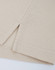 A close-up of a beige cotton/poly pique polo shirt, highlighting the stitched hem and sleeve detail.