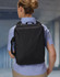 A black utility laptop bag is worn on the back of a person dressed in a checked shirt. The bag has a logo.