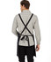 A black bib apron with crossed straps is displayed on a person wearing a checked shirt. The apron features a logo.
